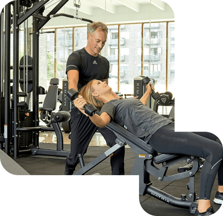 Mand hjælper kvinde med armtræning i fitnesscenter